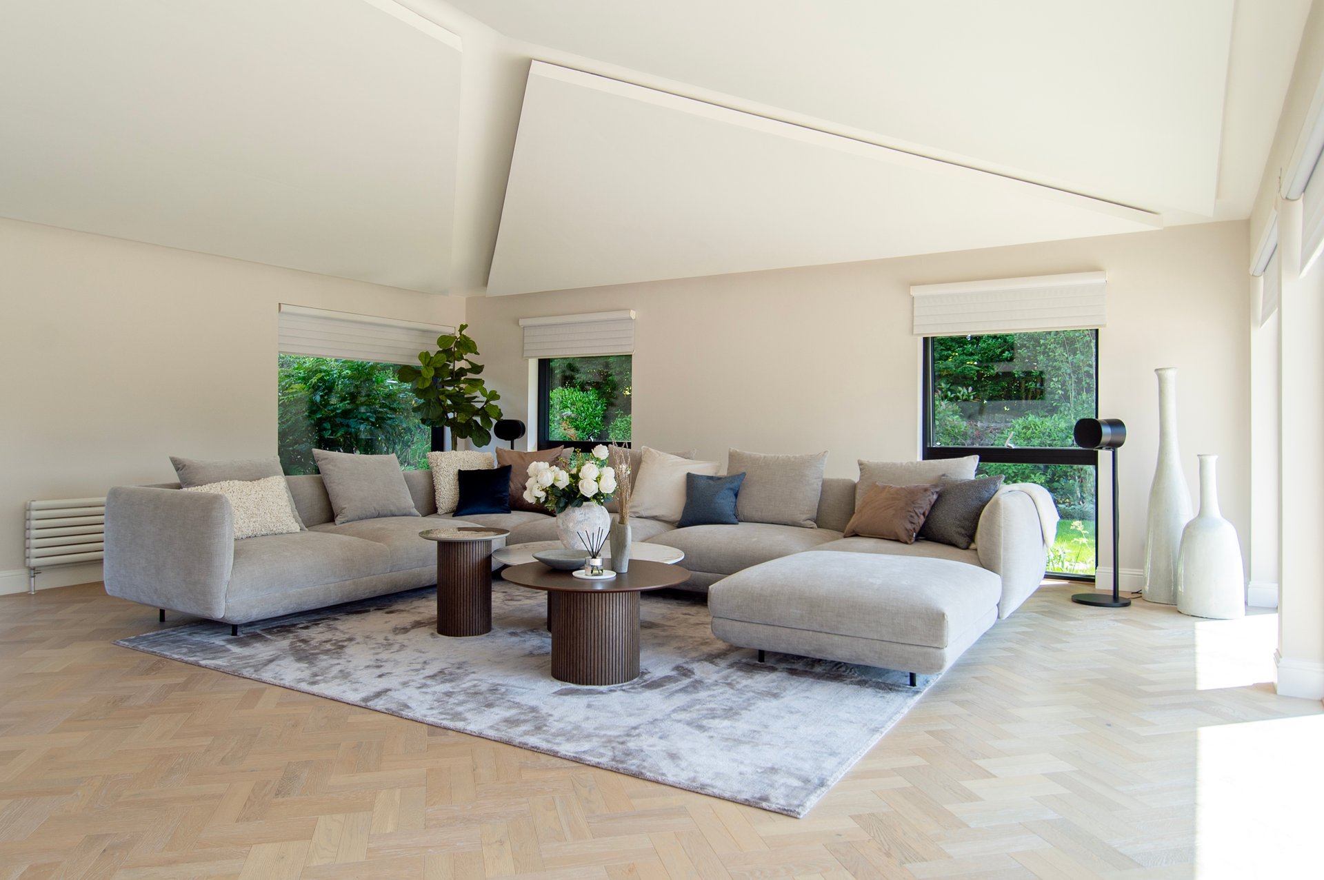 Großes Modulsofa mit Récamiere, Kissen in Grau und Braun, zwei runden Couchtischen und Teppich vor bodentiefen Fenstern