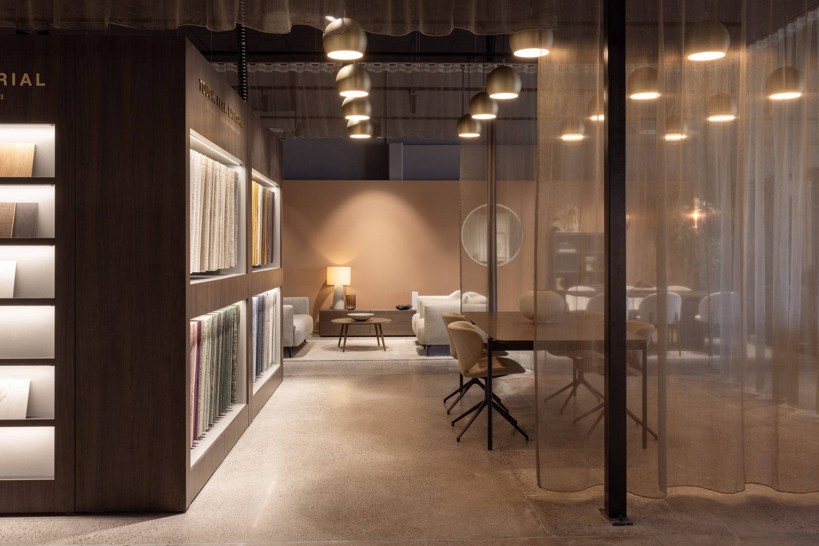 Weißes Sofa mit Sessel, rundem Couchtisch und Hocker vor einer Materialwand im Showroom