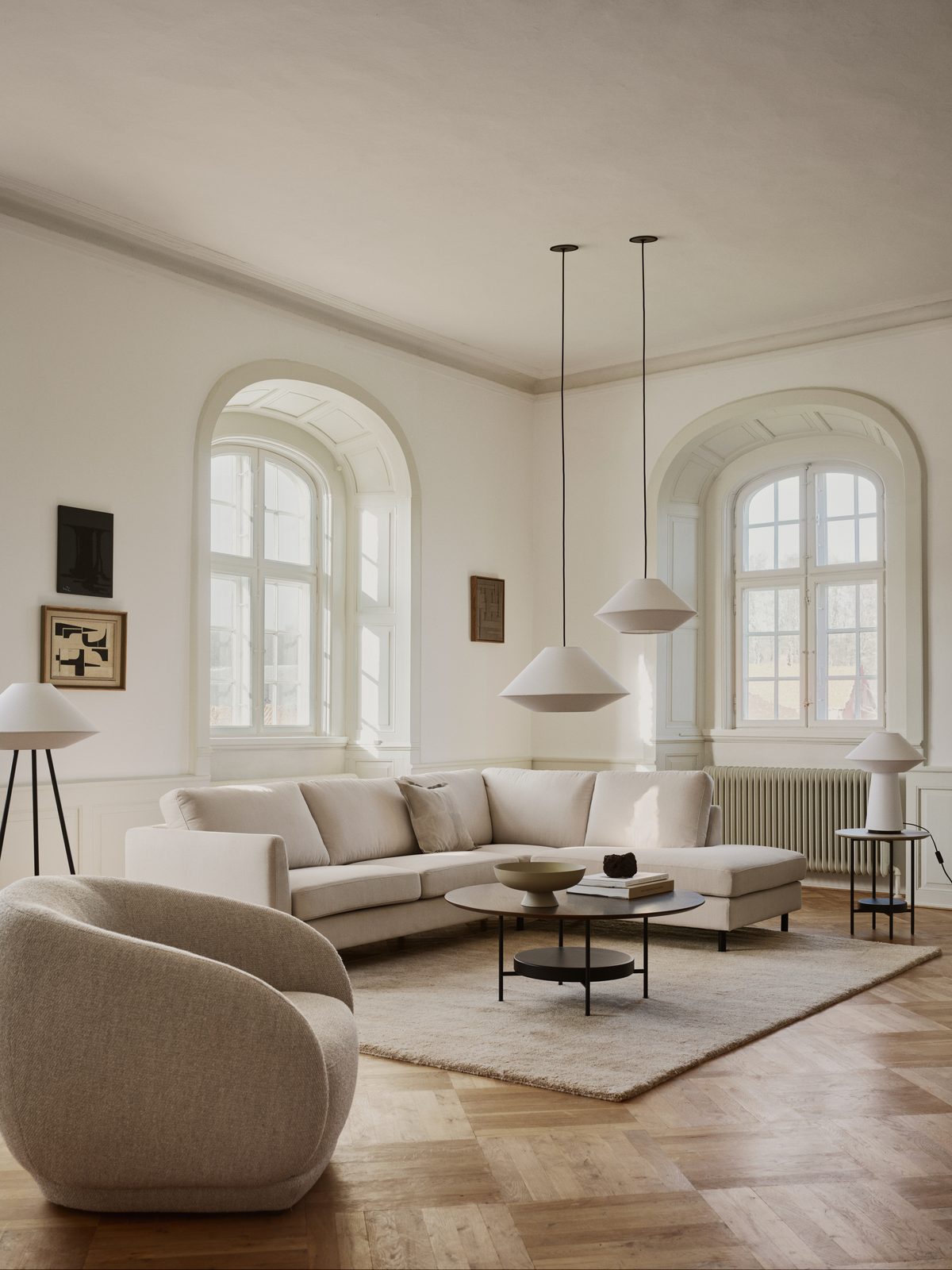 Ecksofa mit Récamiere und rundem Sessel in einem Altbauzimmer mit Rundbogenfenstern