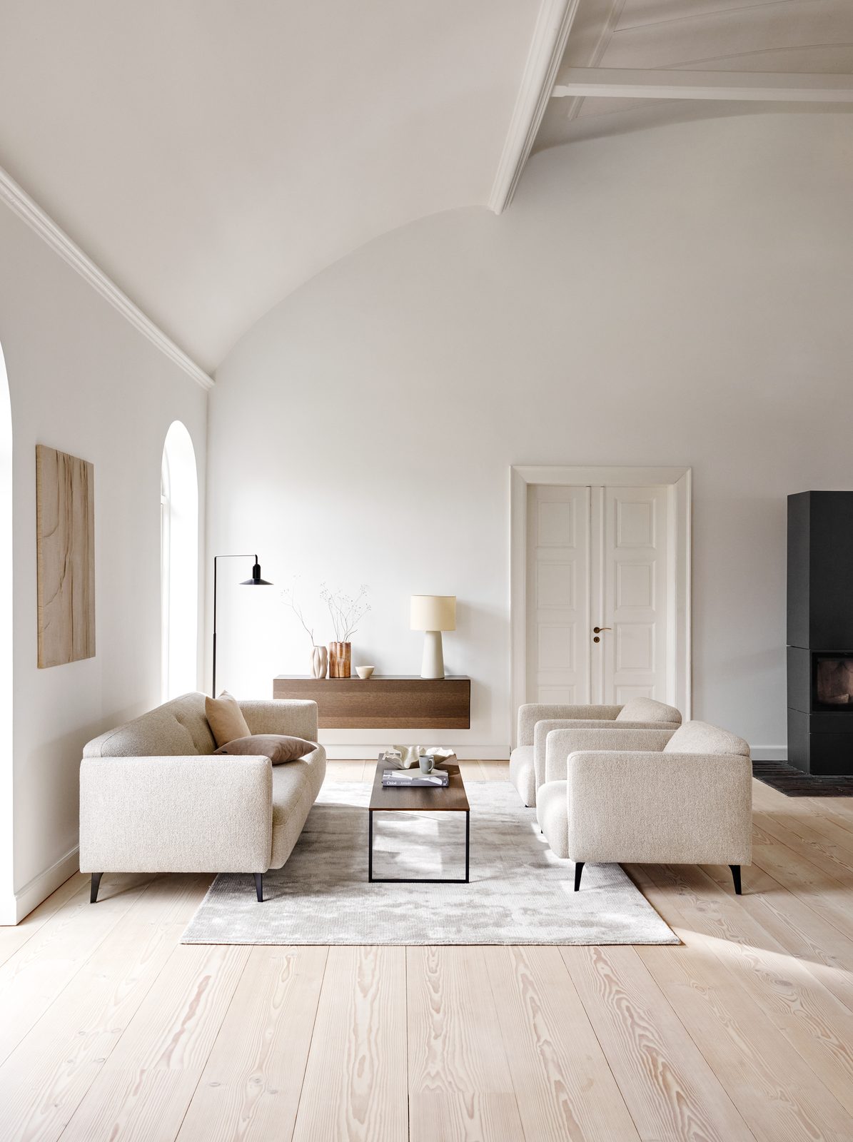 Helles Wohnzimmer mit Tonnendecke, beigem Sofa, zwei Sesseln und schwebendem Sideboard