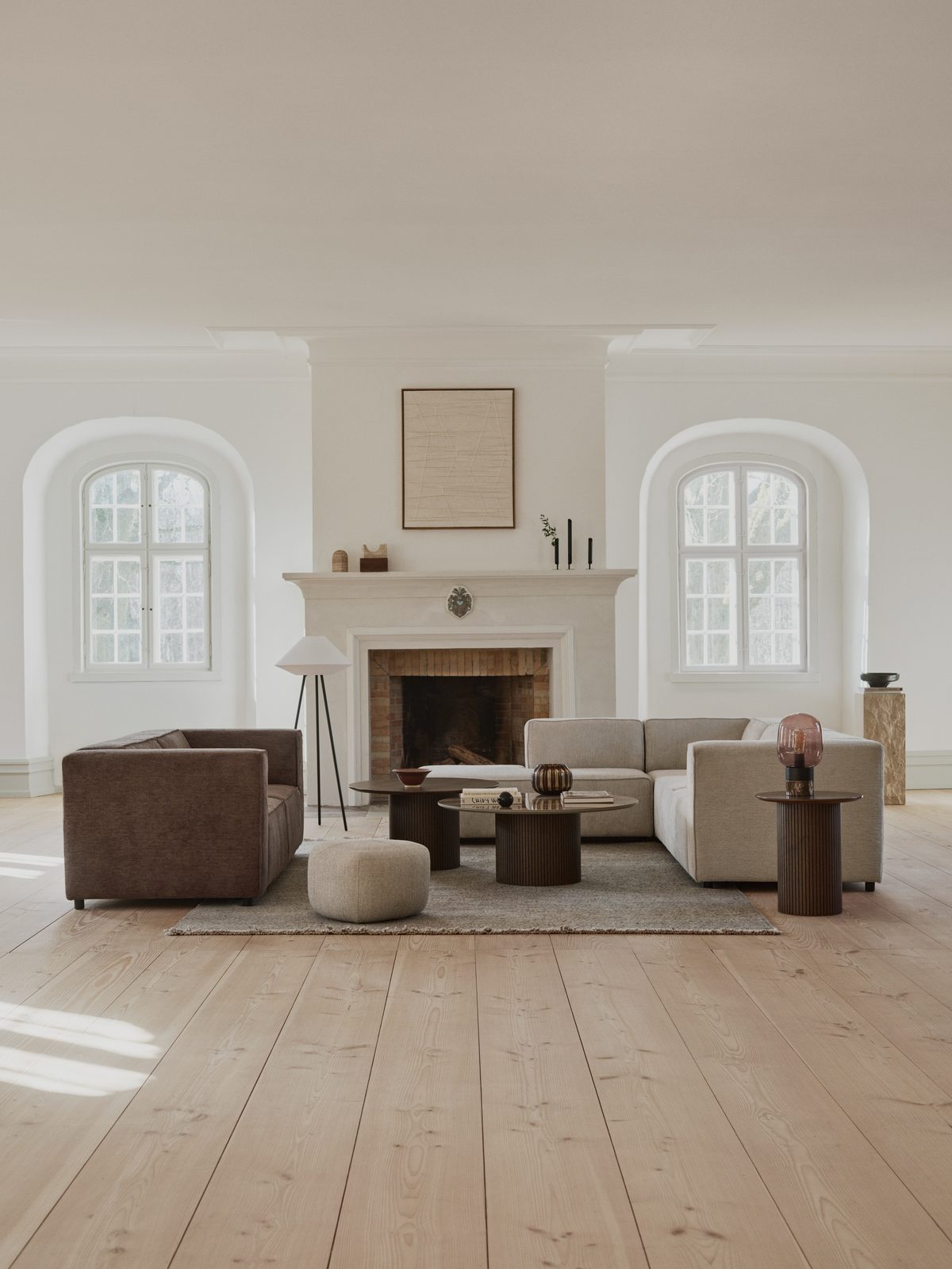 Modulares Sofa und brauner Sessel um einen offenen Kamin, davor runde Beistelltische