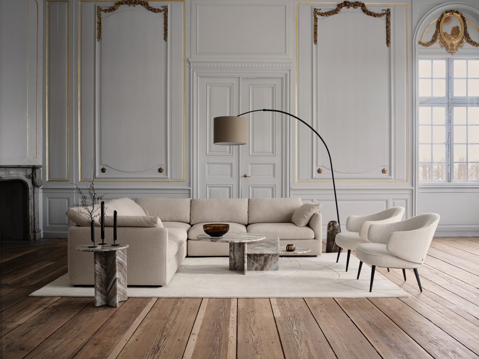Großes Ecksofa in Beige vor Stuckwand, dazu Marmortische und zwei Sessel